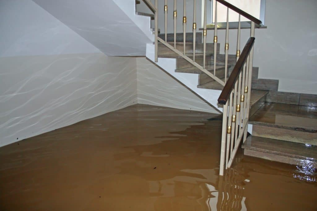 A home interior is severely flooded with muddy water covering the floor and surrounding a staircase.
